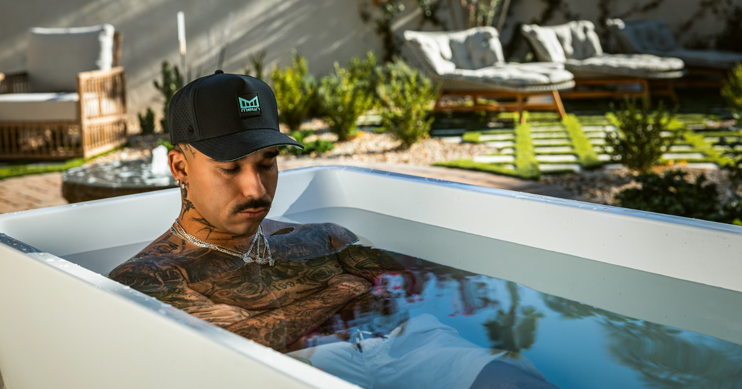 A man wearing the melin Odysea Stacked Hydro hat in Aqua Splash, lounging in a cold plunge tub
