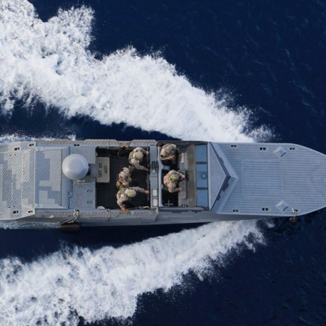 Top-down view of a military ship with personnel on a blue ocean.