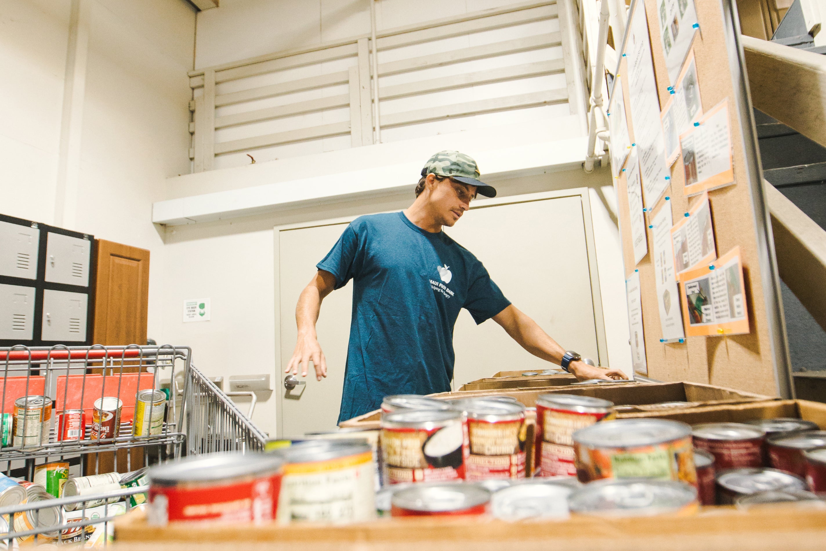 Person organizing canned goods in a pantry setting as part of a giveback initiative with the Maui Food Bank