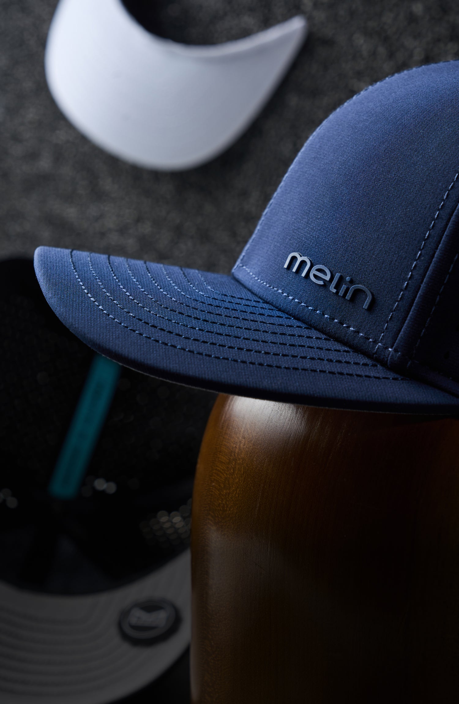 The side view of the melin Compass Hydro in Navy, set against the backdrop of a workshop where melin hats are being constructed